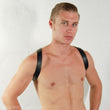 Load image into Gallery viewer, A shirtless blonde man is shown from the chest up, standing in front of a white wall. He wears The Contender Leather BDSM Chest Harness. The black straps wrap over his shoulders.