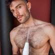 Load image into Gallery viewer, A shirtless man with dark hair, facial hair, and chest hair stands against a red and black background. He holds the wand with the electrode comb from the Kinklab Neon Wand® Electrosex Kit.