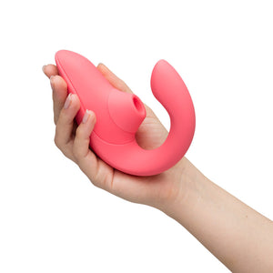 A person's hand cradling the pink version of a Womanizer Blend suction vibrator against a white background. 