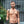 Load image into Gallery viewer, A brunette man wearing the black leather Contender chest Harness and a black thong poses facing away from the camera. The harness forms an X shape on his back with a silver metal O-ring in the center.
