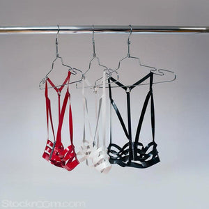 Three latex halter cage bras, one in red, one in white, and one in black, are shown hanging on clothes hangers from a metal rod. 